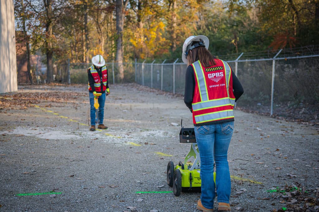 An image of two individuals scanning an outdoor surface, checking for underground utilities.